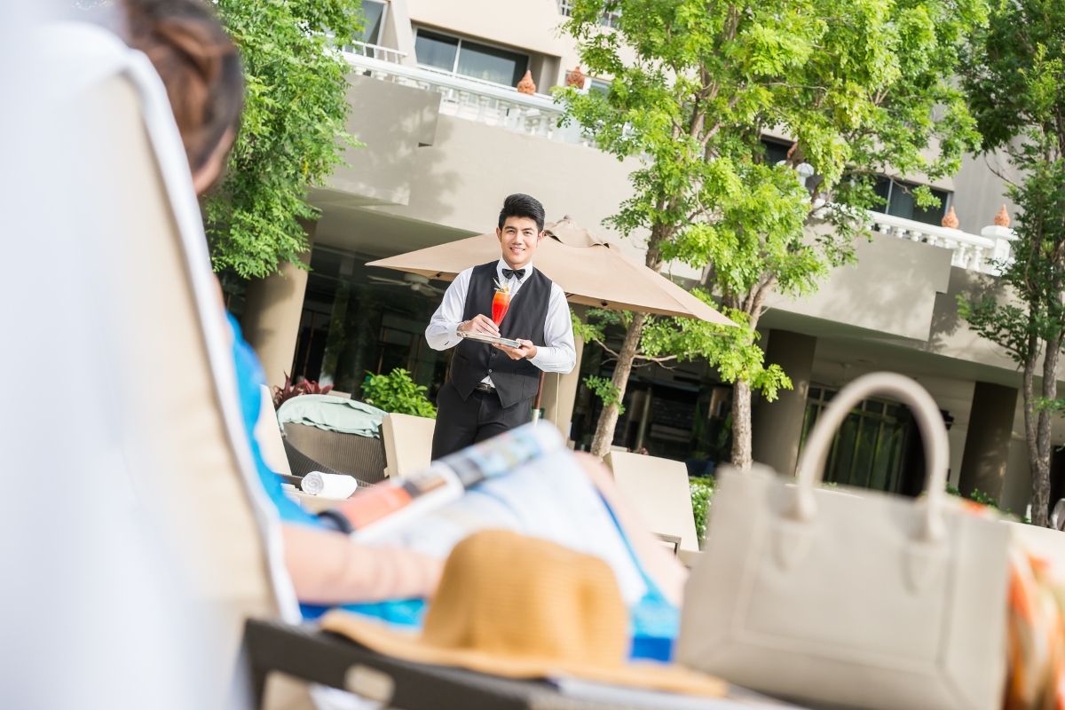 hotel butler serving a drink to guests by the pool